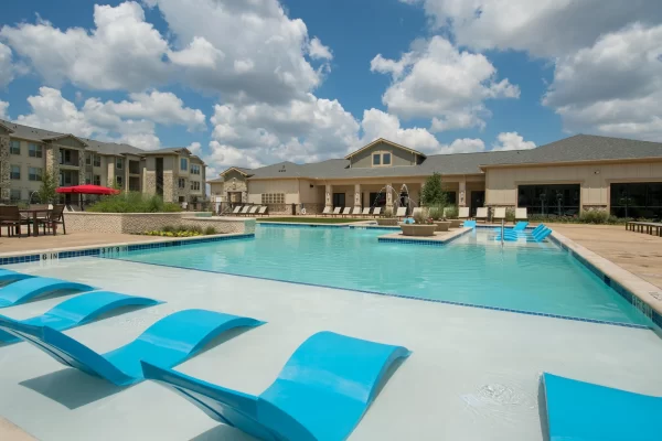 Resort-style pool with built-in lounge areas surrounded by an expansive sundeck with poolside lounging, private cabanas, and the apartment homes in the background