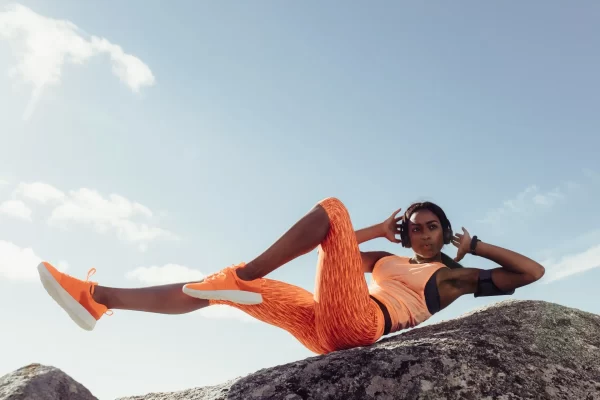 Woman in all orange workout clothes doing an ab workout on a rock